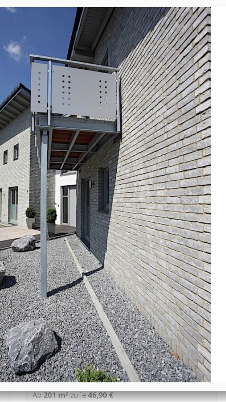 Modern building facade with balcony made of perforated metal over gravel path.