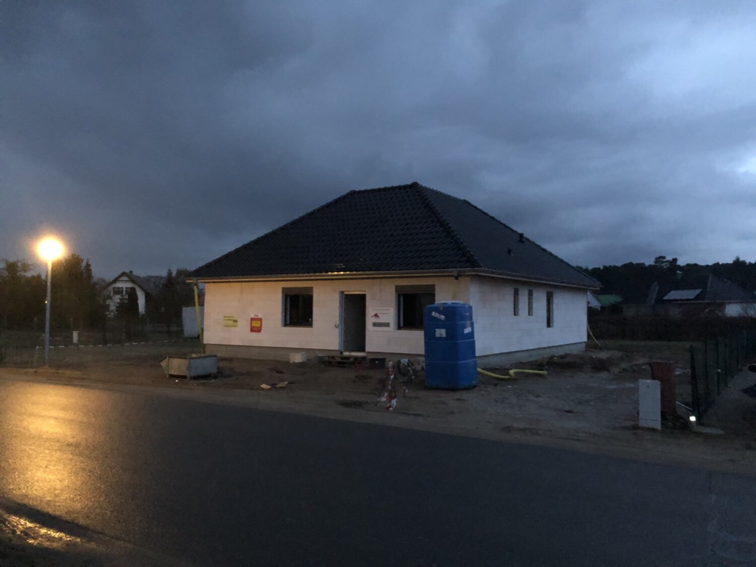 Under construction: white shell structure with dark pitched roof, blue cistern, street lamp on the left.