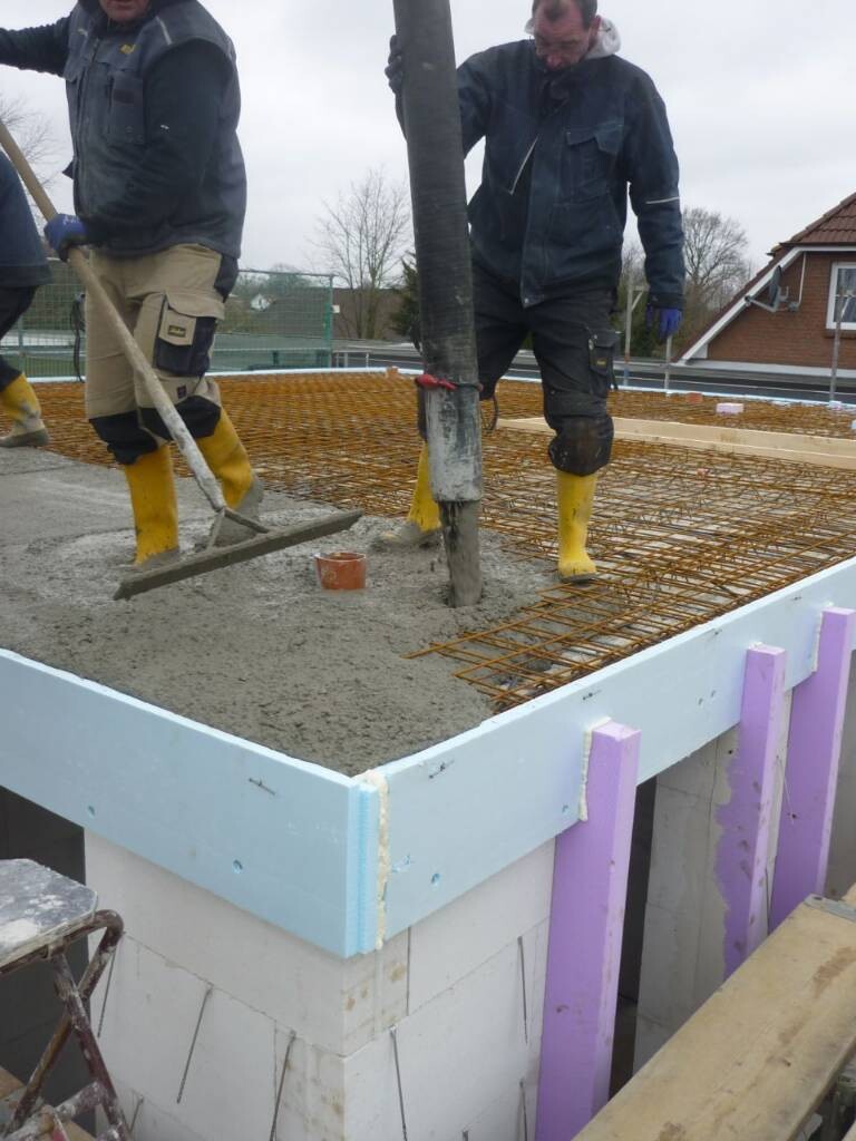 Two construction workers pouring fresh concrete over reinforcement steel in a formwork.