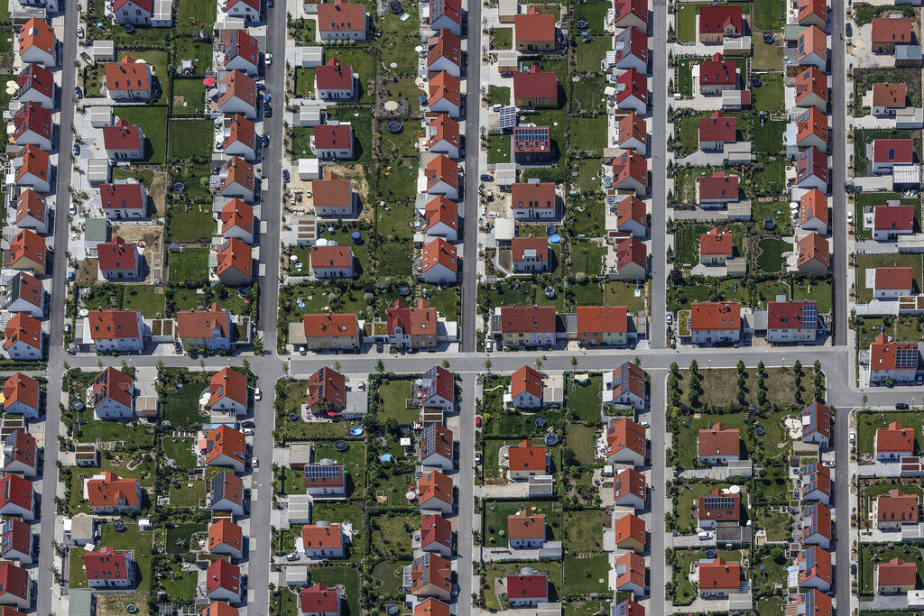 Aerial view of a residential neighborhood with many red roofs, green gardens, and a grid-like street pattern.