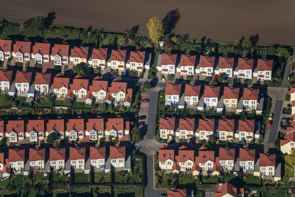 Bird’s-eye view of terraced houses with red roofs and green gardens.