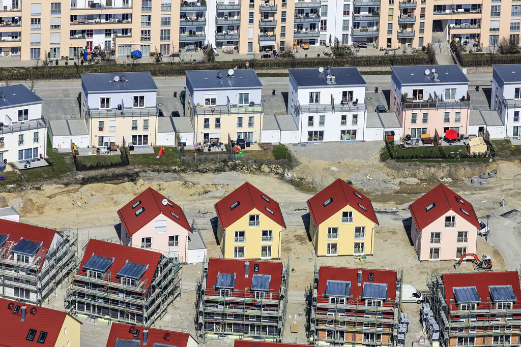 New development with red roofs and scaffolding; behind it, multi-family houses.
