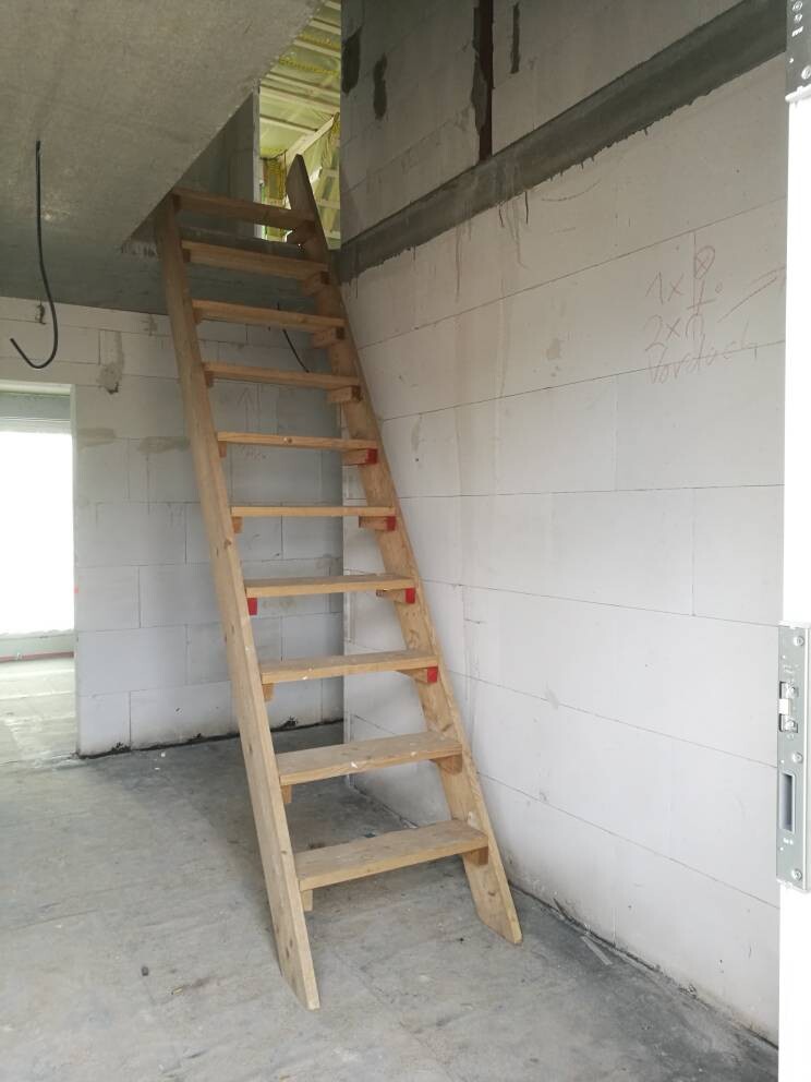 Temporary wooden staircase in an unfinished interior with concrete walls, construction phase.