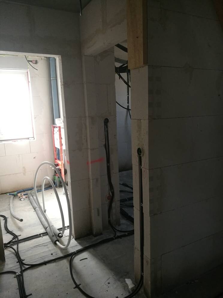 Unfertiger Bauinnenraum mit Betonwänden, schwarzen Kabeln, flexiblen Schläuchen und Fenster.