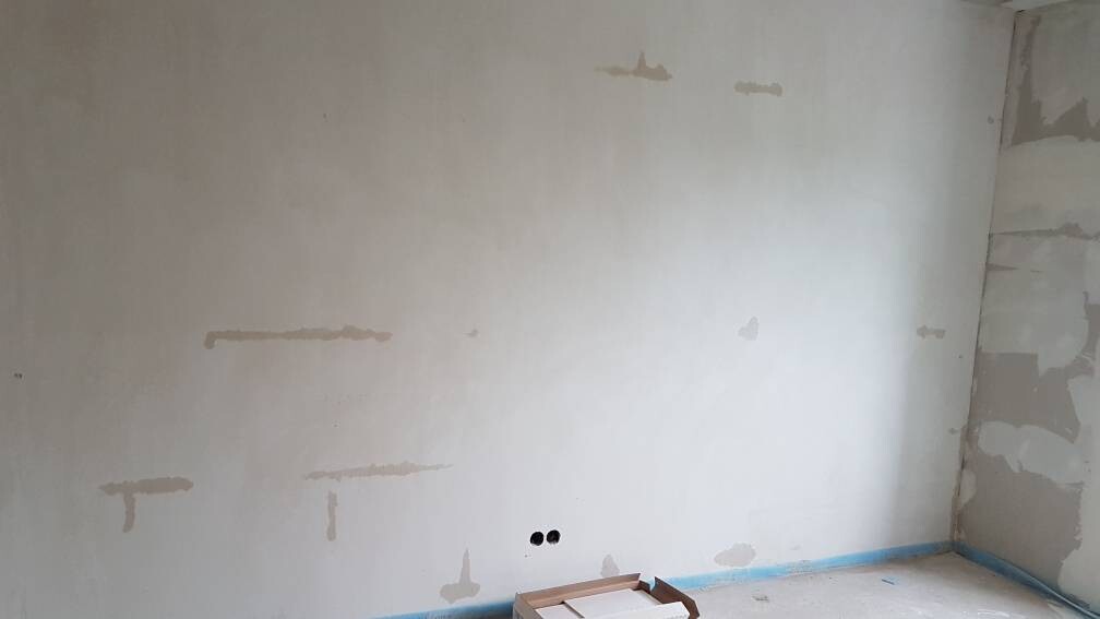 Unfinished interior with repair areas on the wall, two holes, blue skirting board and cardboard box.
