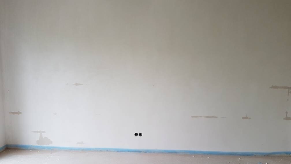 Empty interior: white wall with repair spots, blue baseboard, two round wall openings.