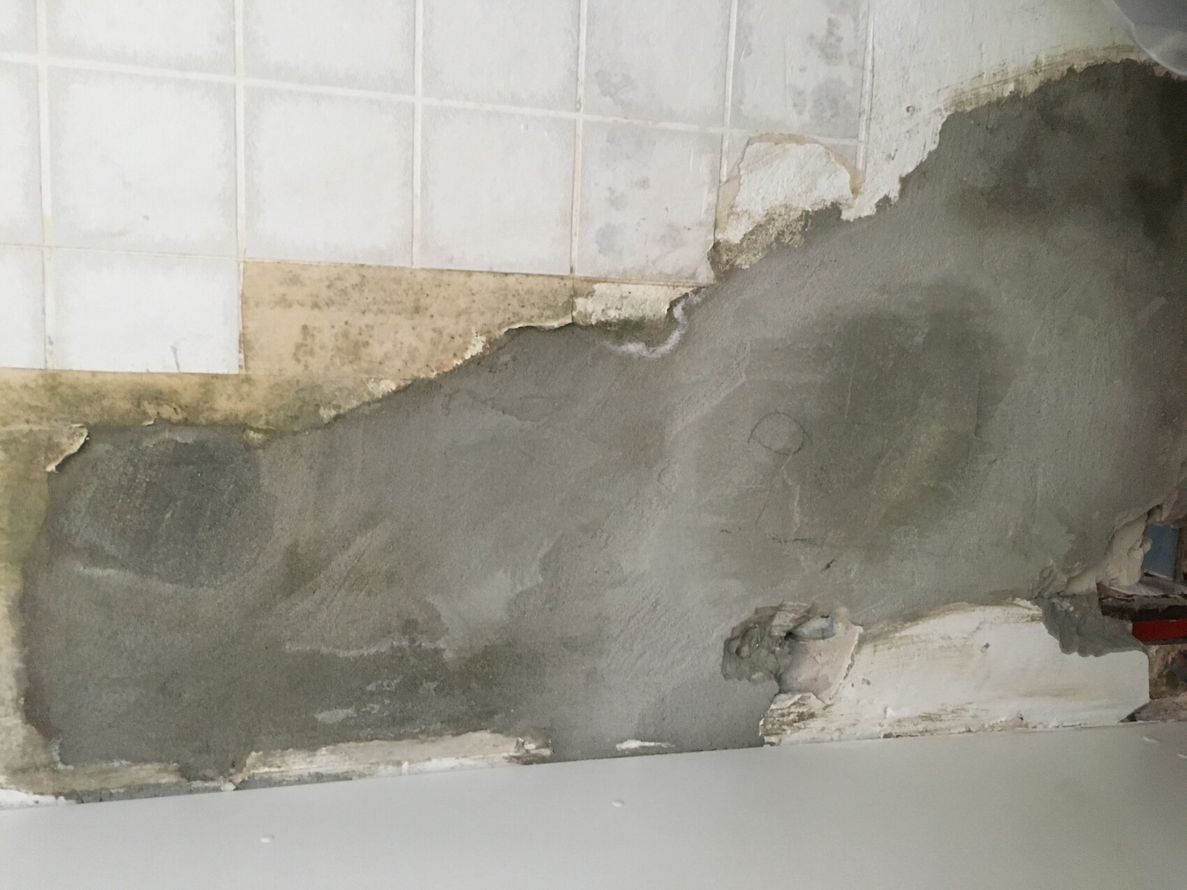 Damaged bathroom wall with torn plaster and tiles, showing need for renovation.