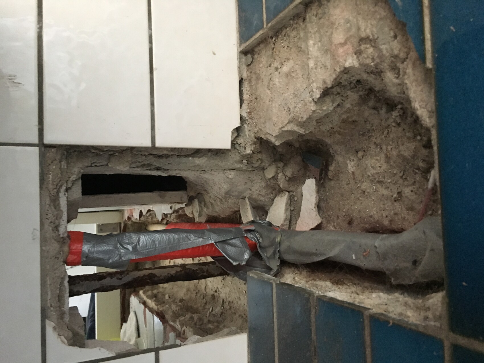Torn-up bathroom floor with exposed pipes and construction work.