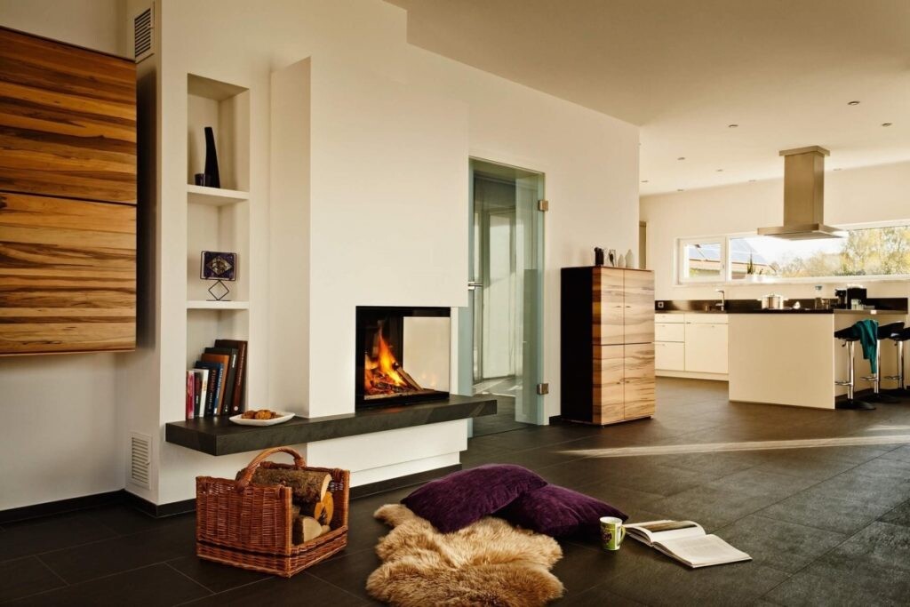 Bright open living space with fireplace, kitchen island, and seat cushions on dark floor.
