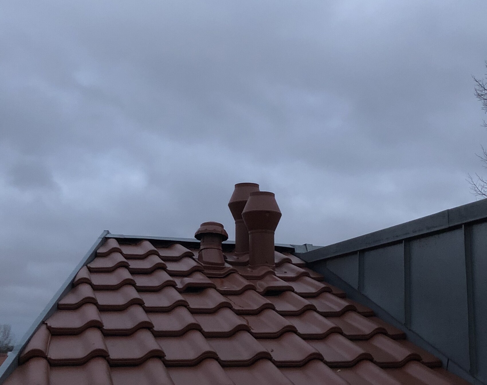 Red tiled roof with several chimneys under clouds
