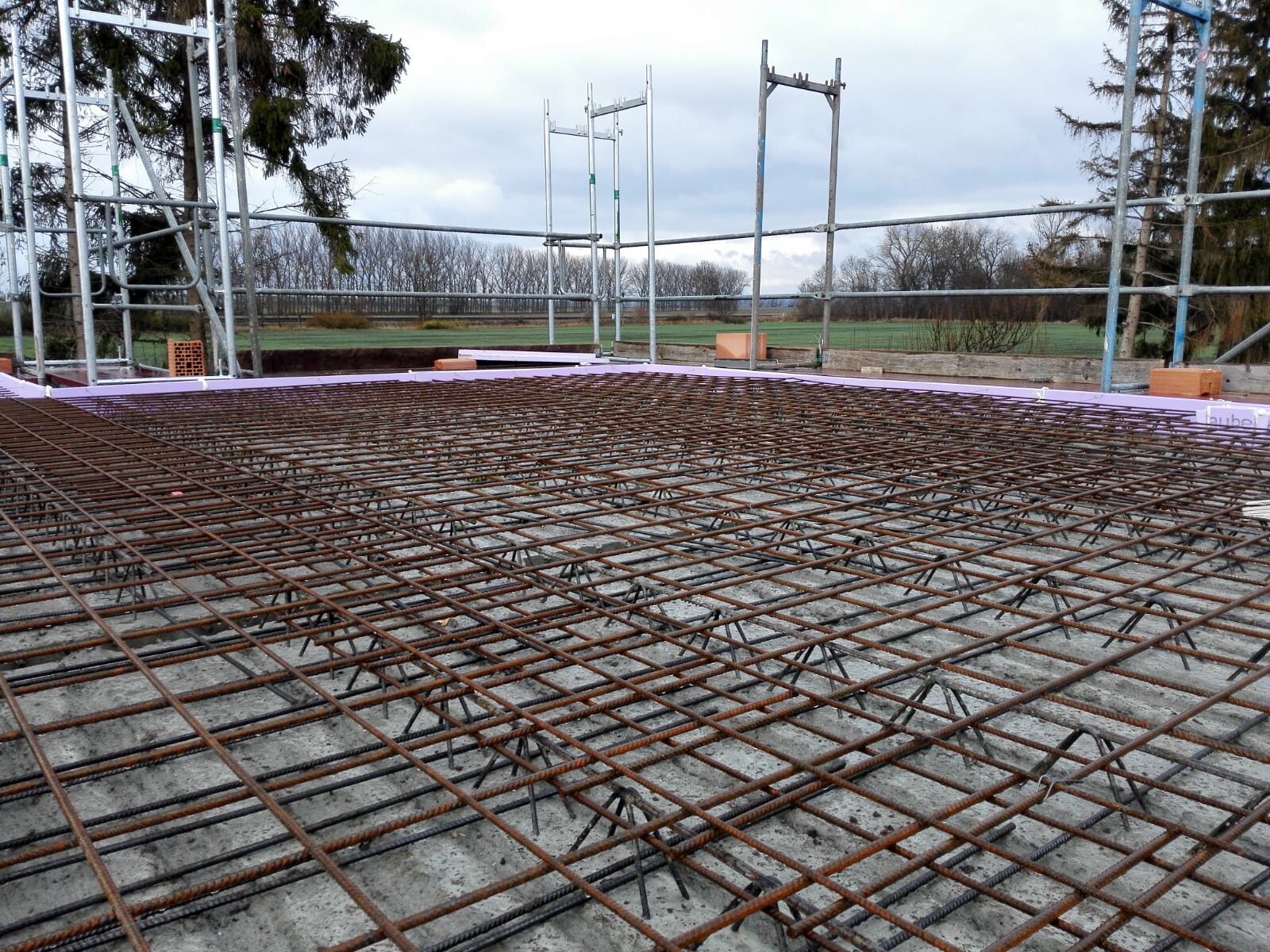 Reinforcement steel mesh lying over a concrete slab at a construction site with scaffolding.