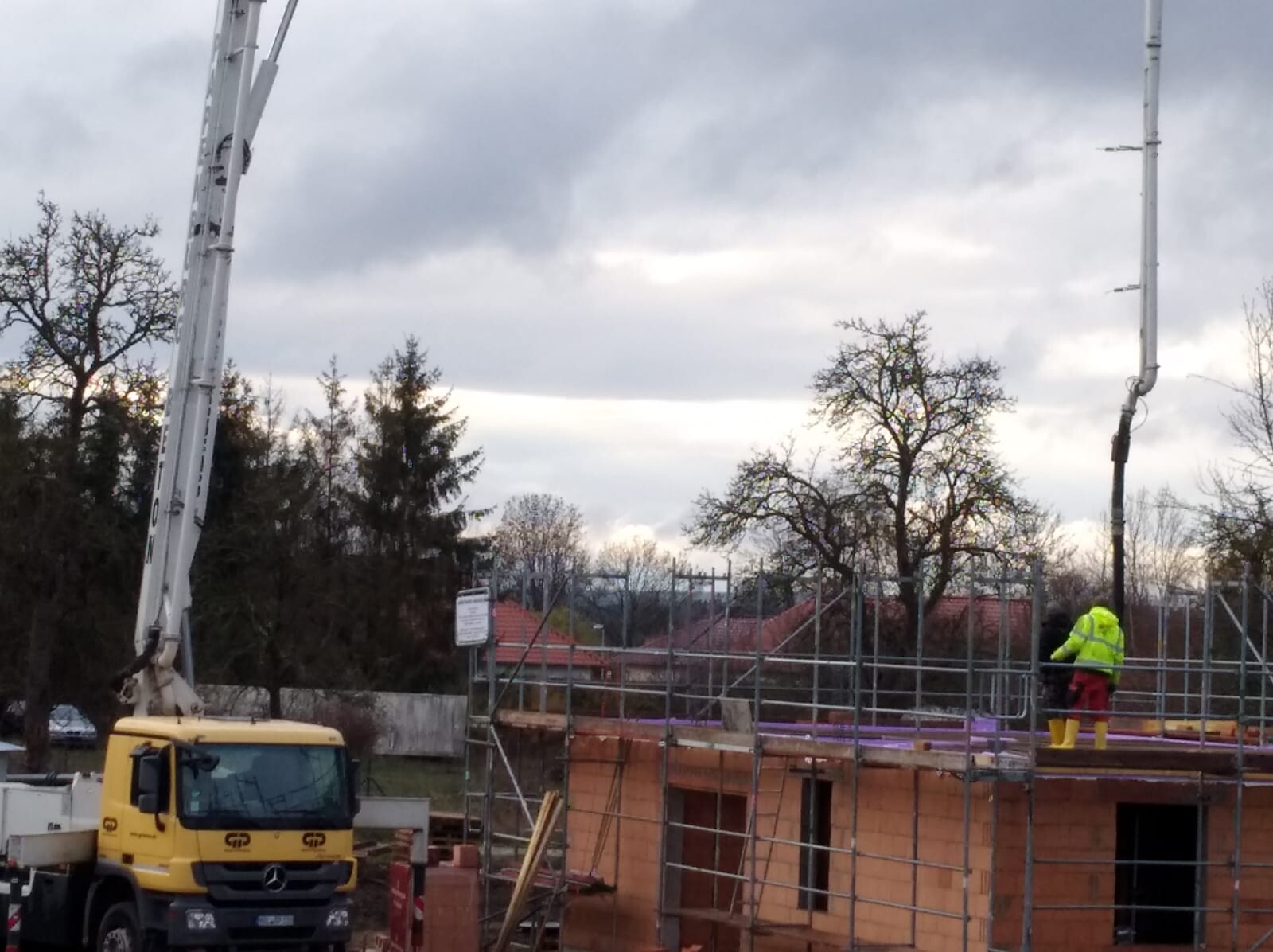 Construction vehicle with crane next to scaffolding, two construction workers in high-visibility clothing on a work platform.