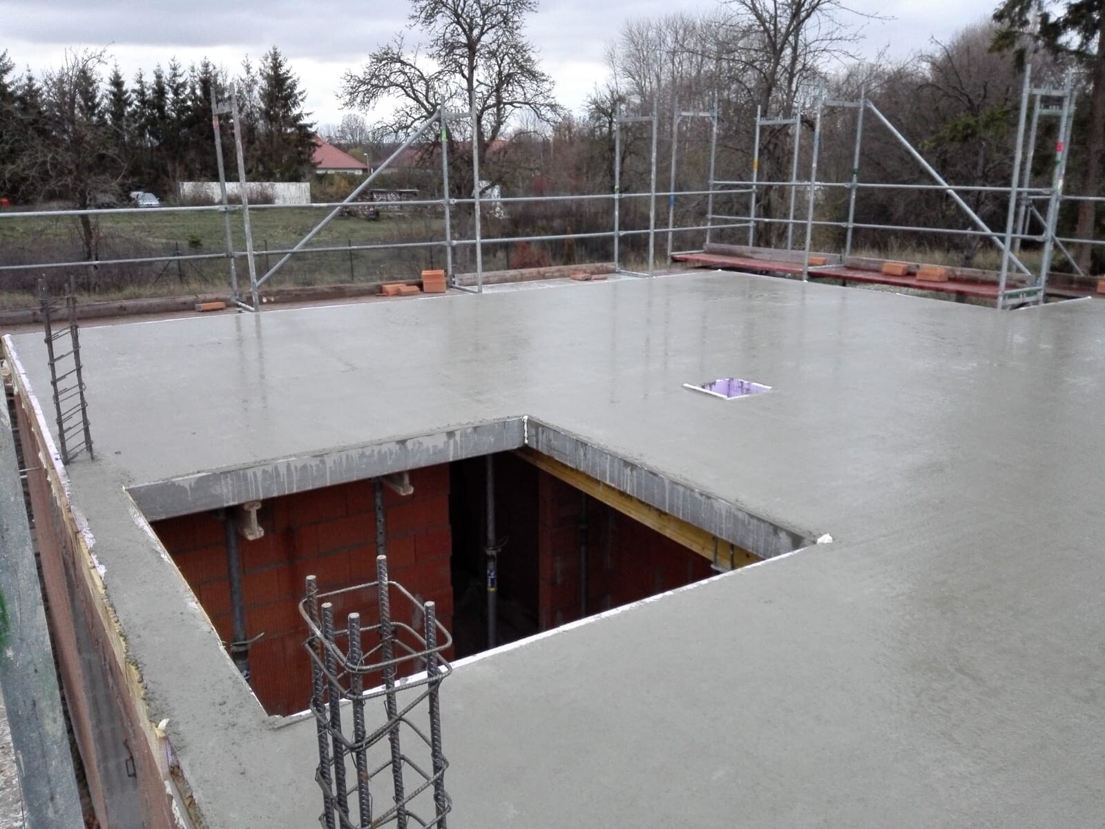 Freshly poured concrete ceiling at construction site, hole in the slab, surrounding scaffolding.