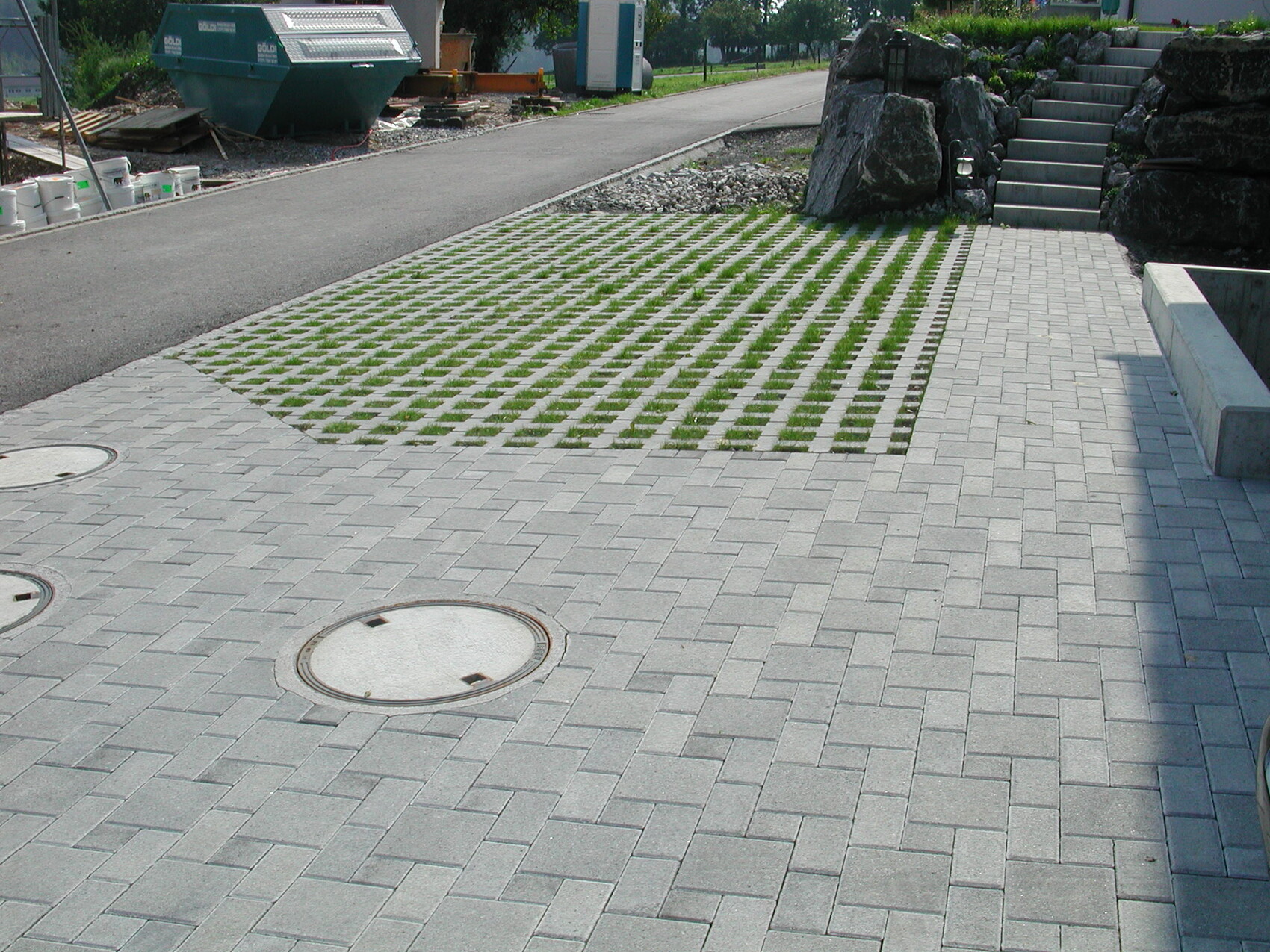Paved area with square-patterned grass grid; construction zone on the left, rock steps on the right.