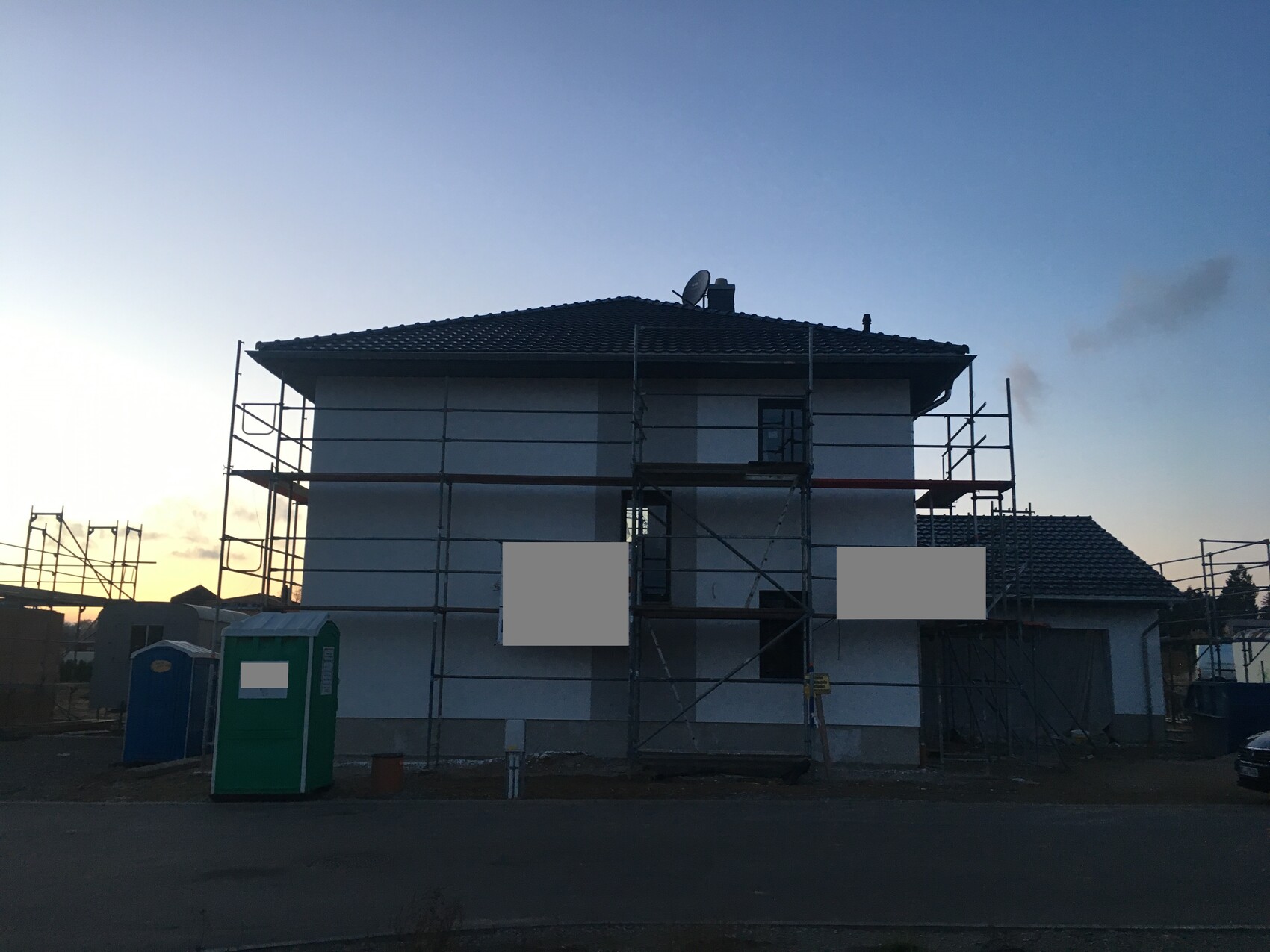 Two-story house under construction with scaffolding and satellite dish at dusk.