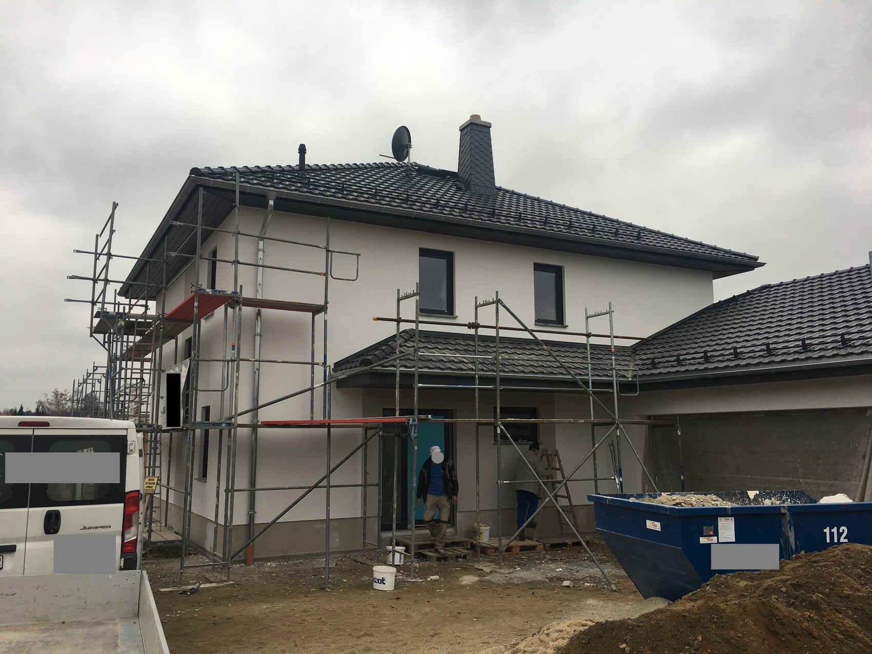 Two-story house under construction with scaffolding, construction workers, and construction debris container.