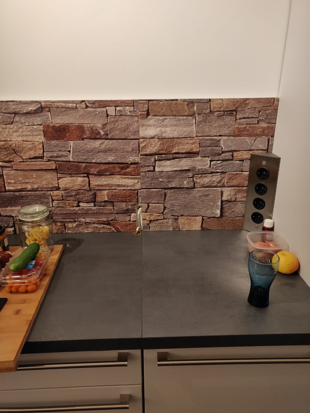 Modern kitchen with gray countertop and stone-look backsplash, fruit on the table.
