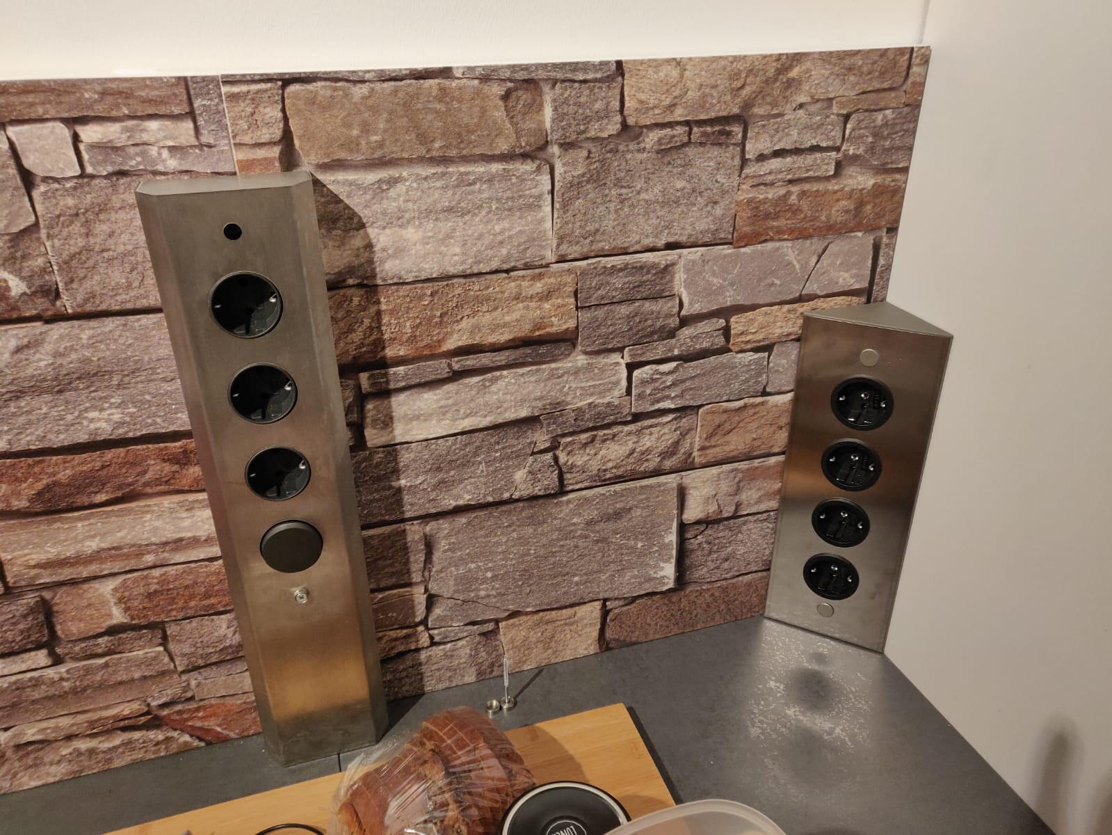 Two stainless steel power strips in front of stone wall in kitchen with bread on the table
