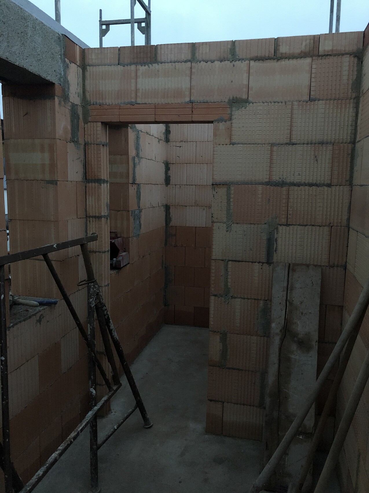 Brick shell with door opening, unfinished walls, construction scaffolding in the foreground.