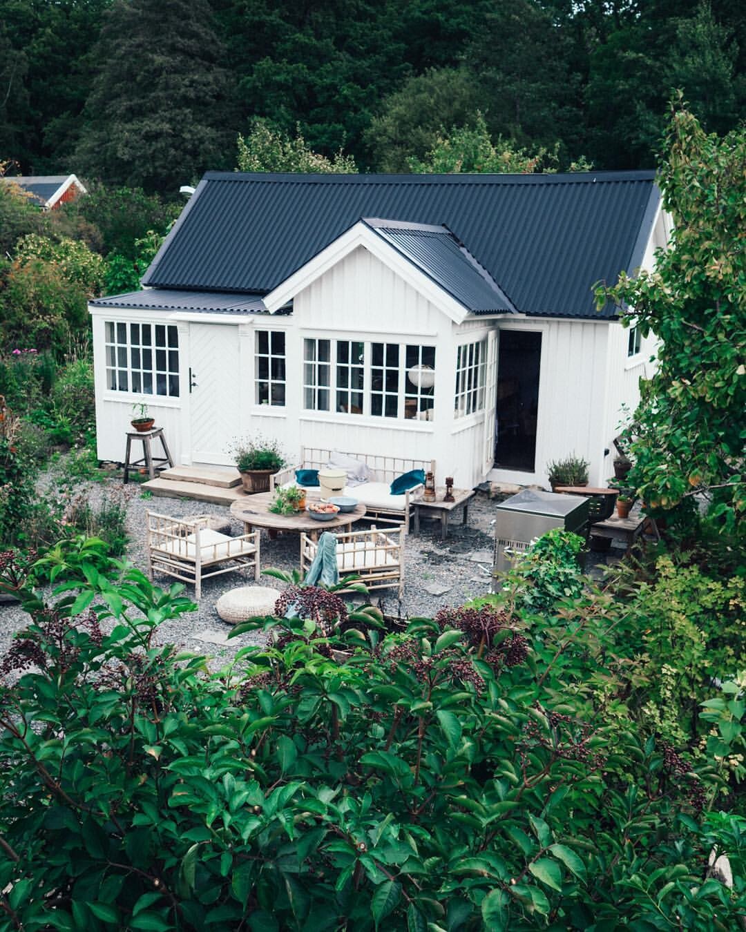 Small white garden shed with dark roof, surrounding garden and seating area.