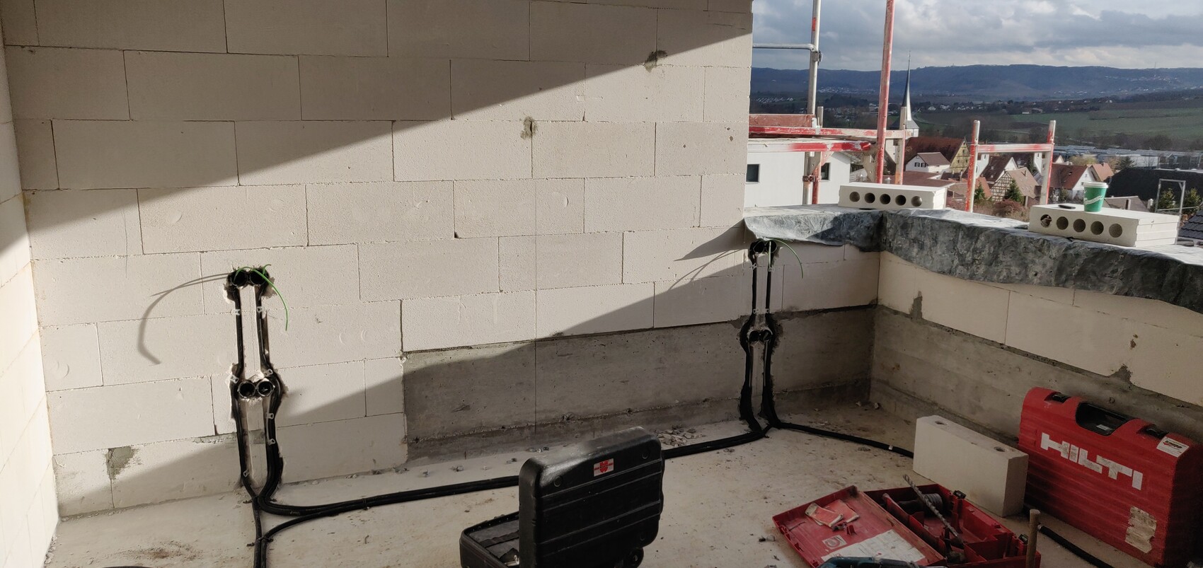 Construction scene on roof terrace: white blocks, cable ducts, cables, toolbox, and Hilti case.