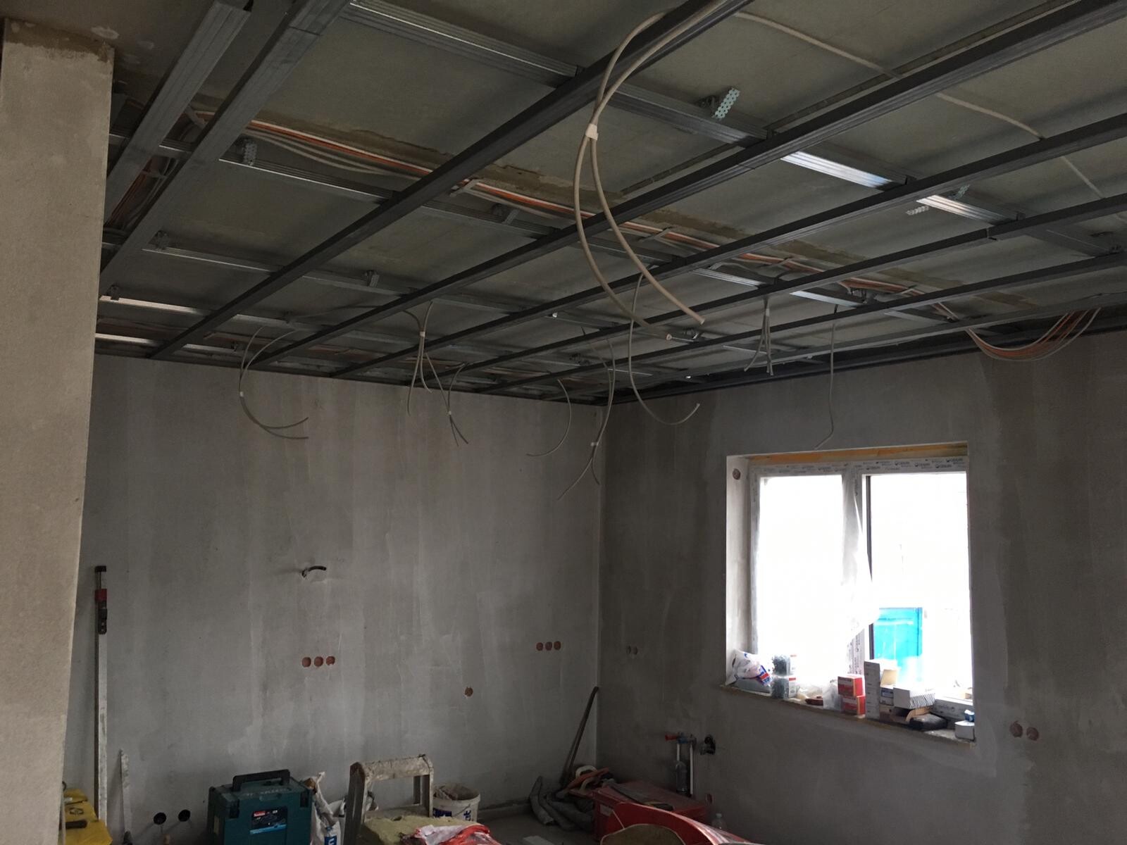 Renovation room with open ceiling, steel beams, loose cables, unfinished walls and window.