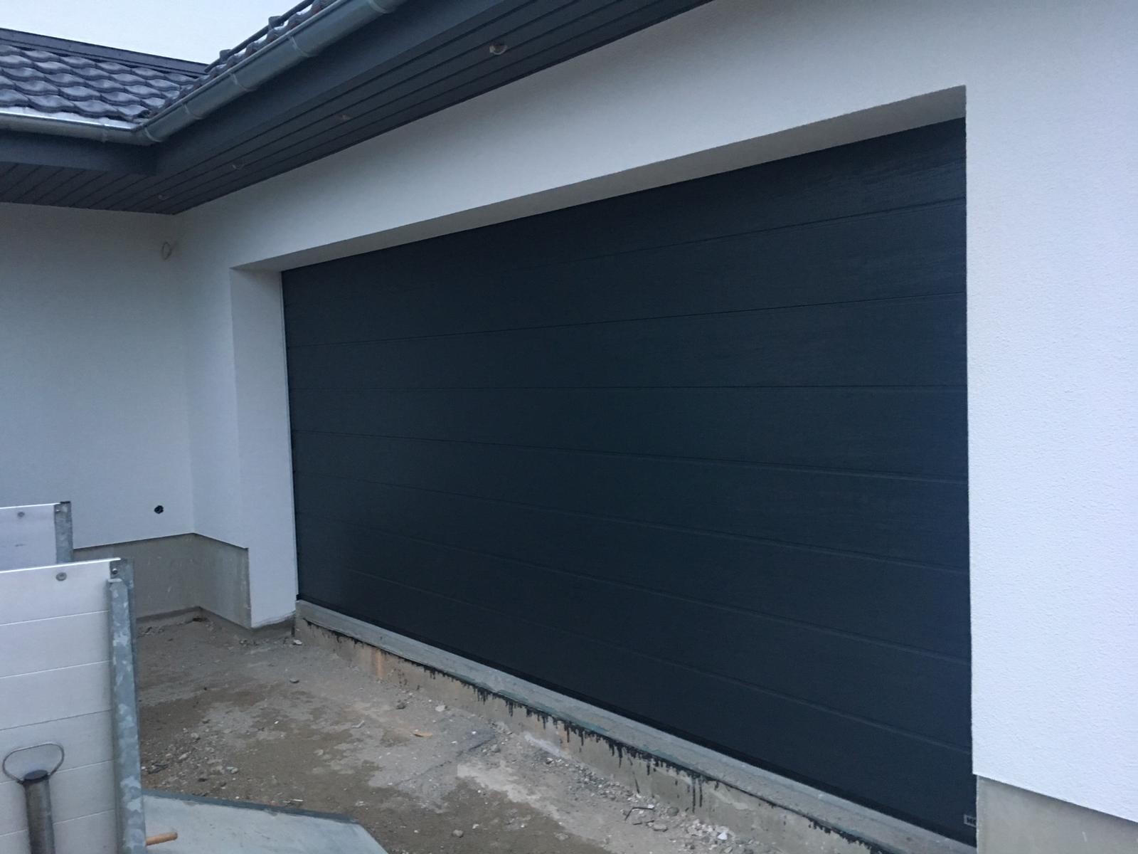 Dark blue garage door on a white house, construction site in front.