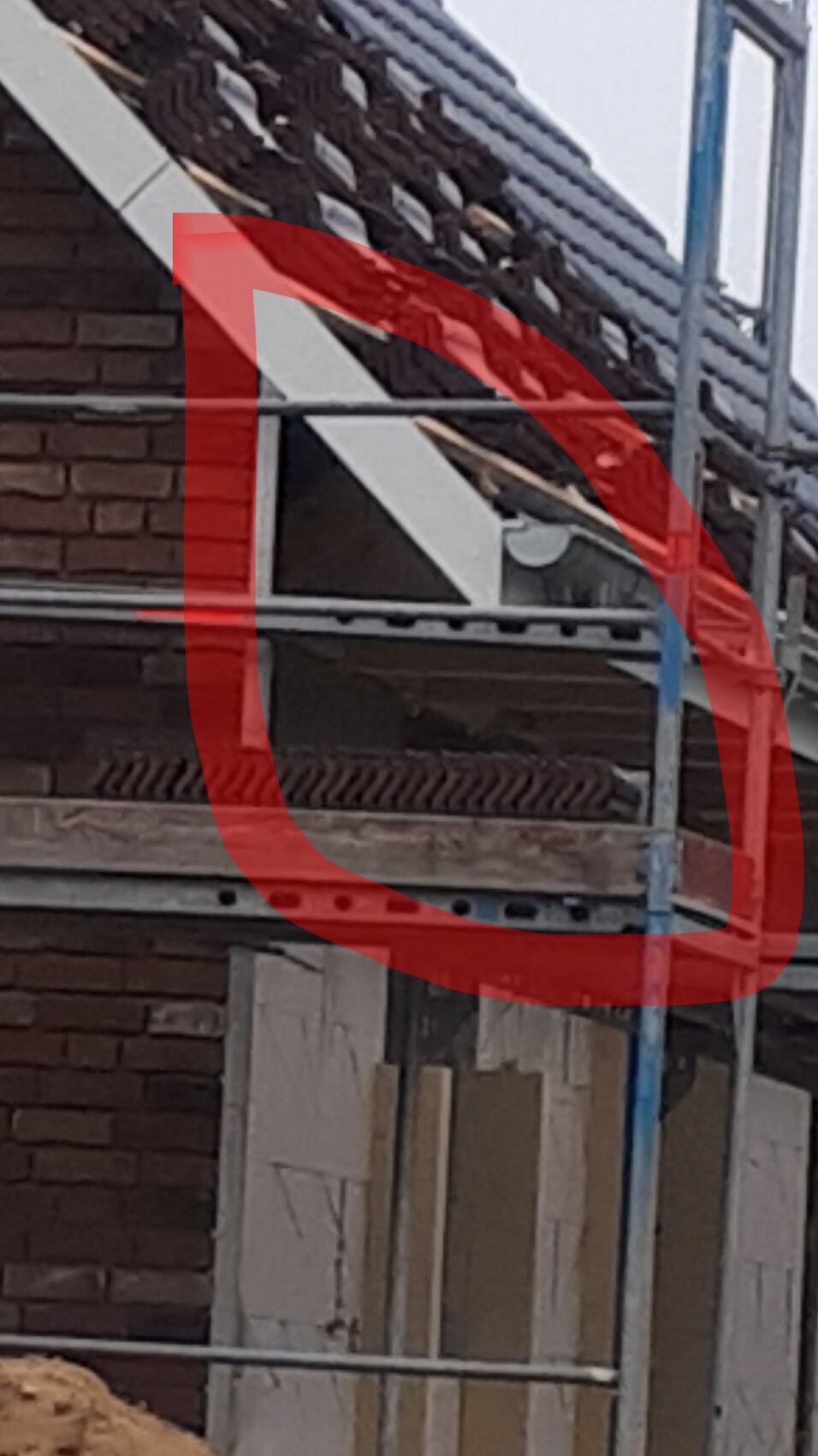Construction site at a house: scaffolding, roof tiles, brick wall, and building materials visible.