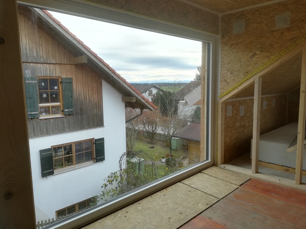 Blick aus dem Dachgeschossfenster auf Garten und Nachbarhaus; Innenraum aus Holzständerwerk.