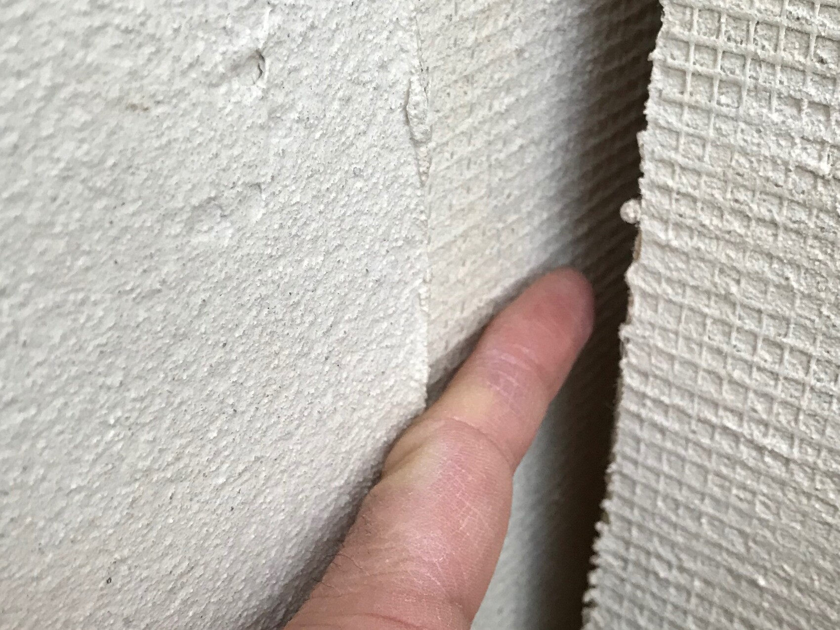 Finger pointing at fine cracks in rough wall joint, indication of construction defect