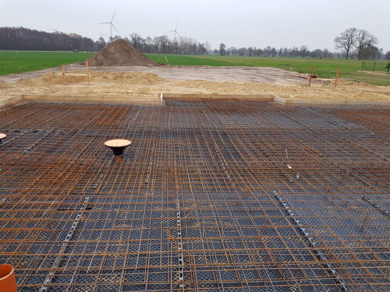 Baustelle mit Stahlbewehrung auf Fundamentplatte; Windräder im Hintergrund.