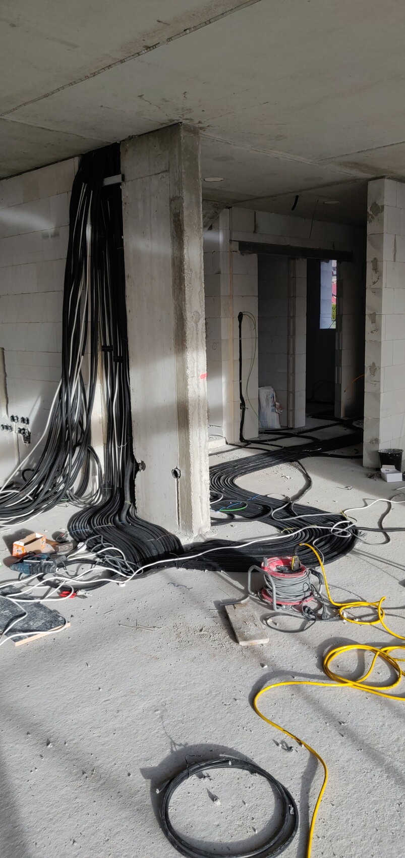 Construction site: Numerous black cable bundles on the floor, concrete walls and support columns.