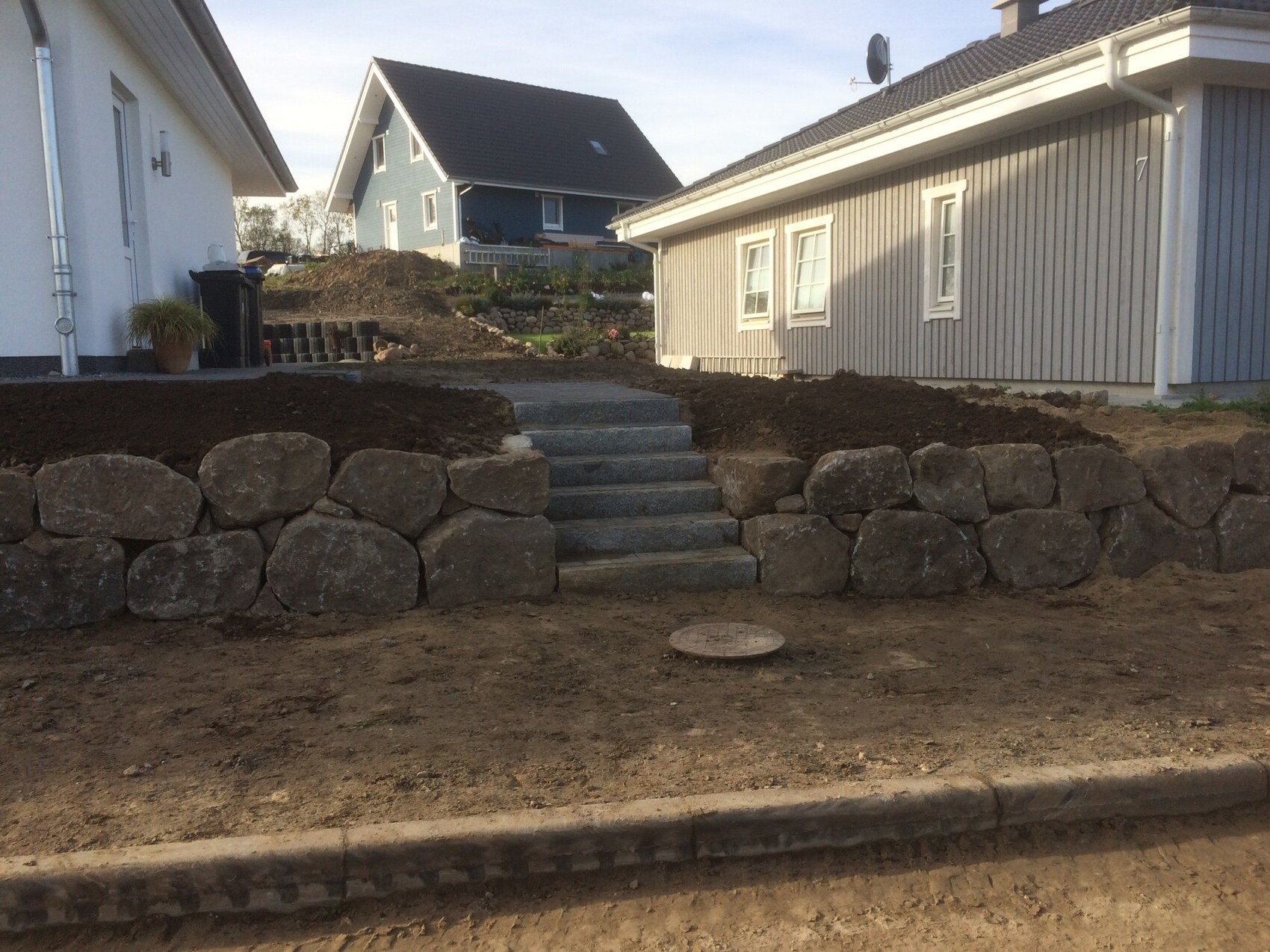 Garten mit Natursteinmauer und Stufen, Bauarbeiten, angrenzende Häuser im Hintergrund