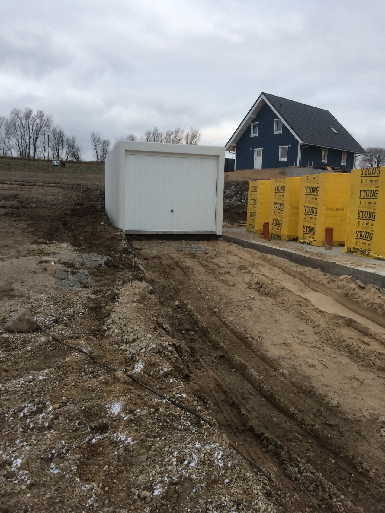 Weißer Bau-Container vor blauem Haus auf der Baustelle; gelbe YTONG-Blöcke stehen bereit