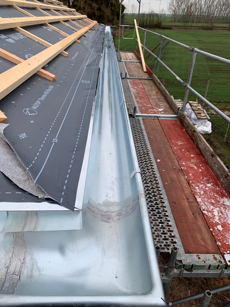 Roof edge: underroof membrane, wooden battens, metal edge flashing, scaffolding platform, field in the background.