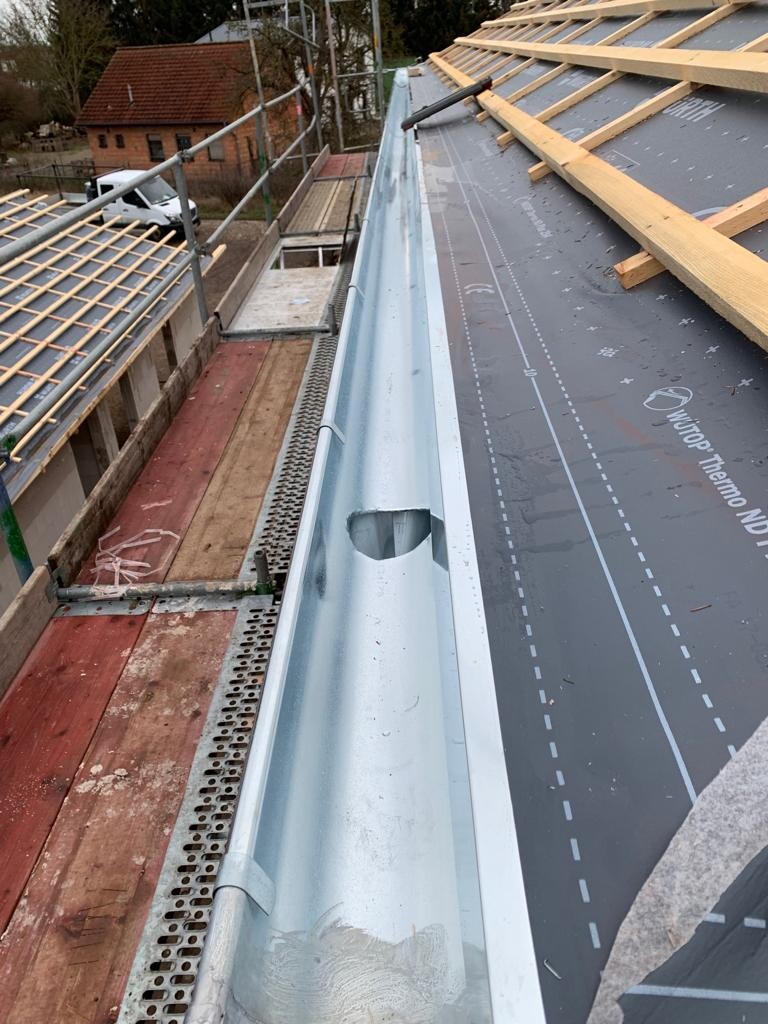 Roof structure at construction site: metal gutter at the roof edge, wooden battens and scaffolding visible