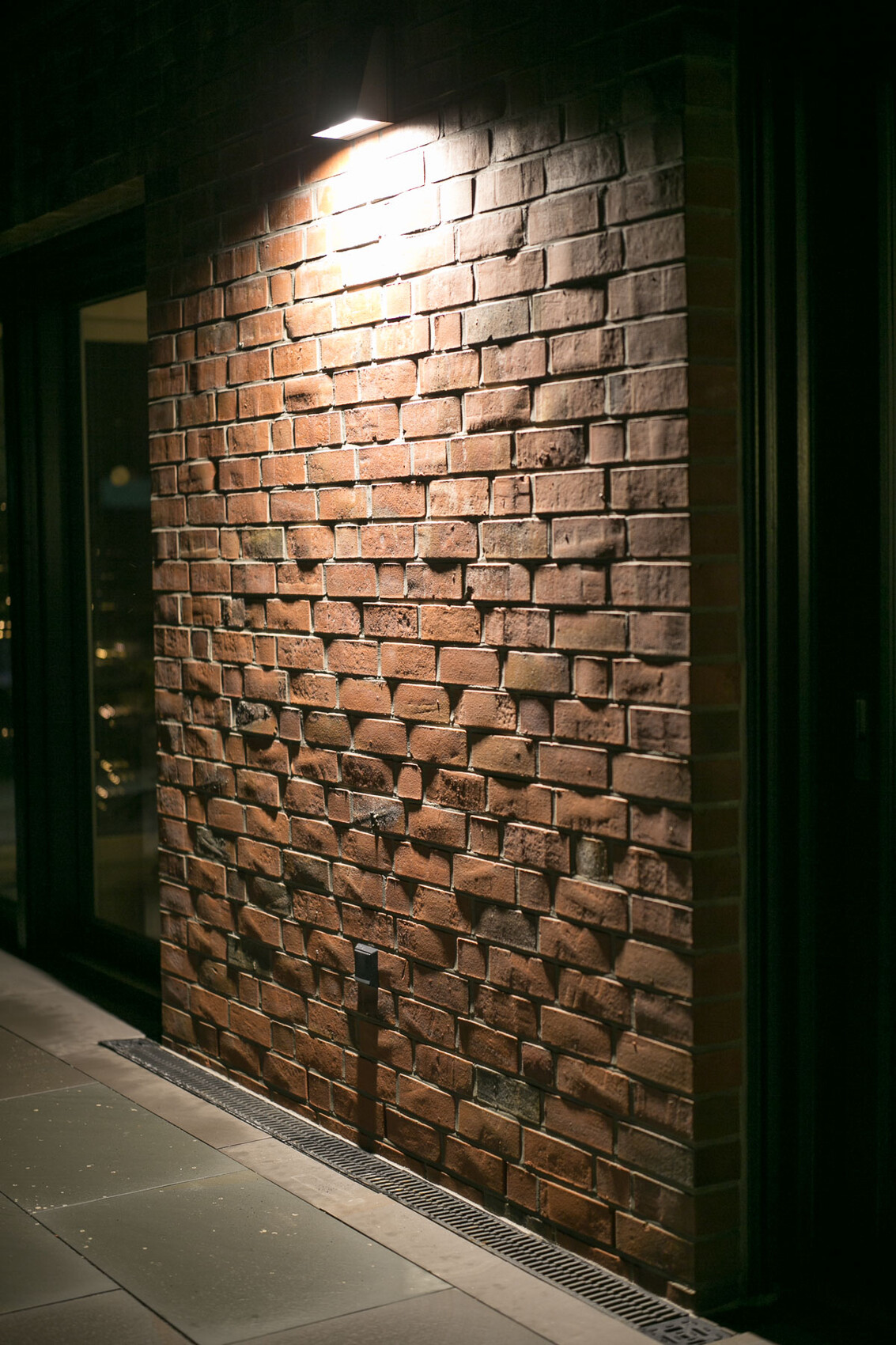 Night shot of a red brick wall, illuminated by an exterior light.