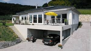 Exterior view of a modern white house with terrace, yellow parasol, and garage underneath.