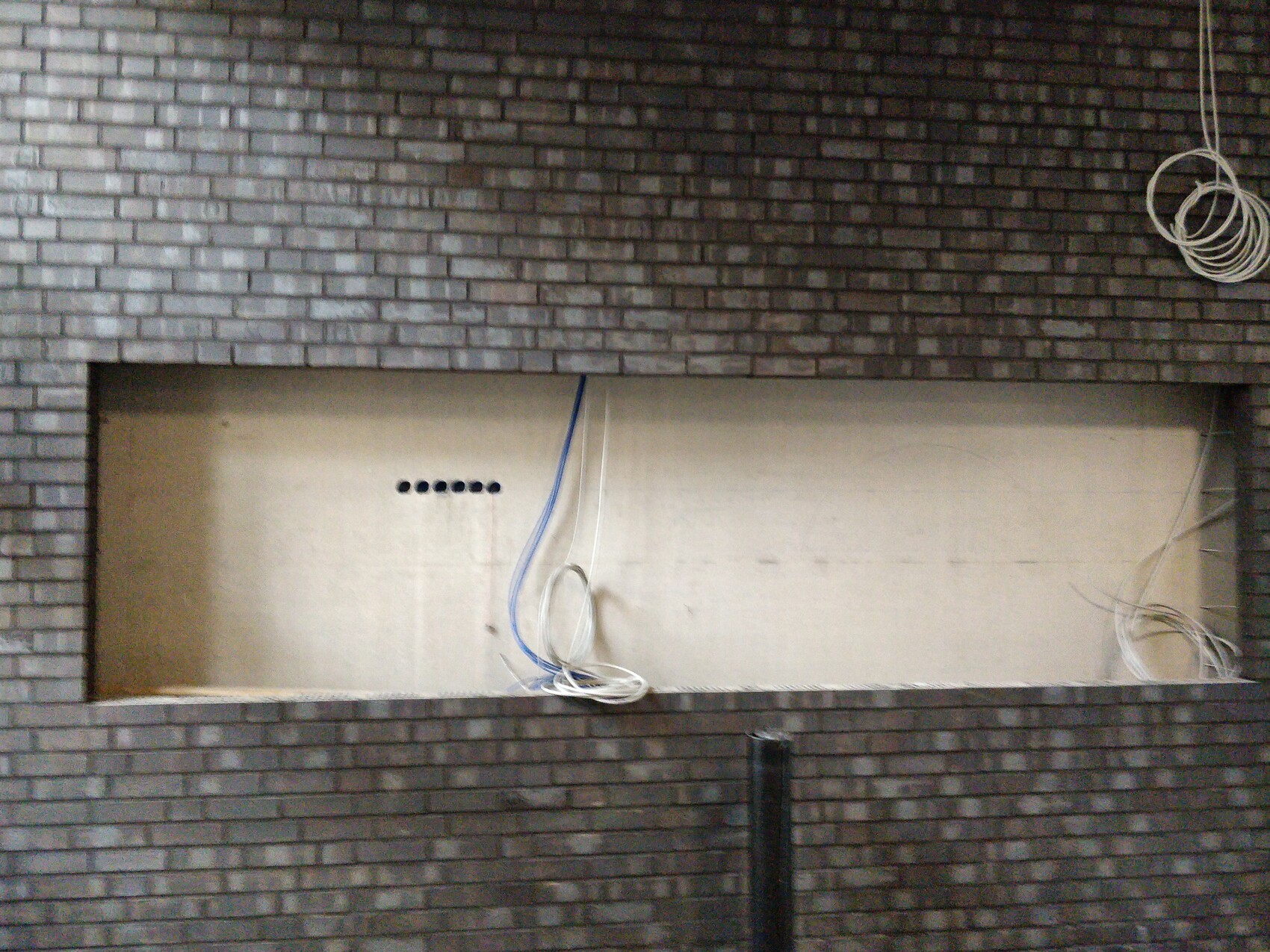 Open wall niche in a brick wall; beige interior surface, loose cable bundles (blue/white) hanging down.