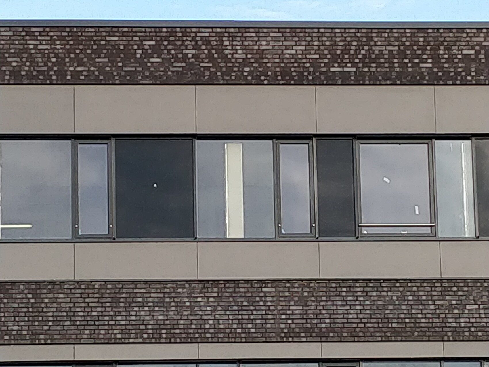 Modern building facade with a row of large windows in light-colored panels, between brick bands.