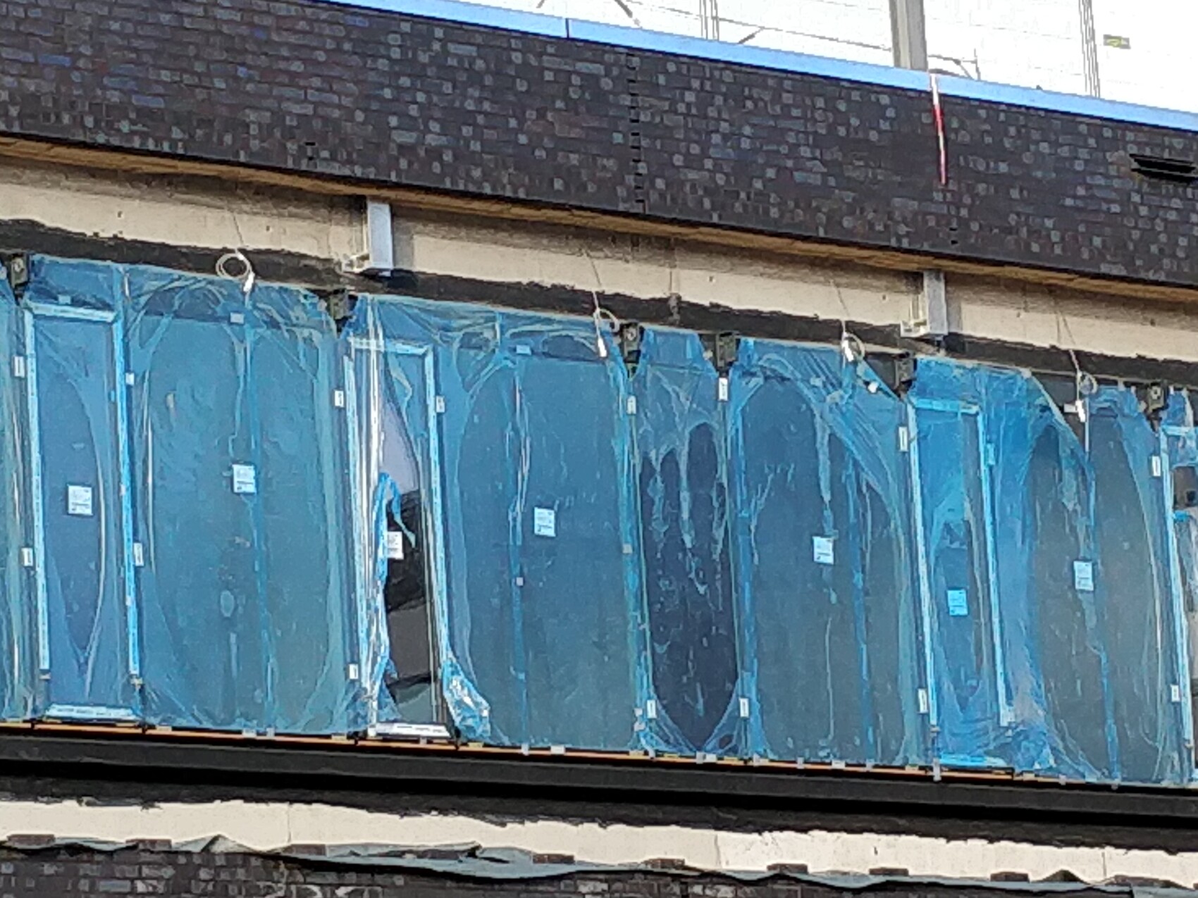 Row of blue glass panels in protective film at a facade construction site