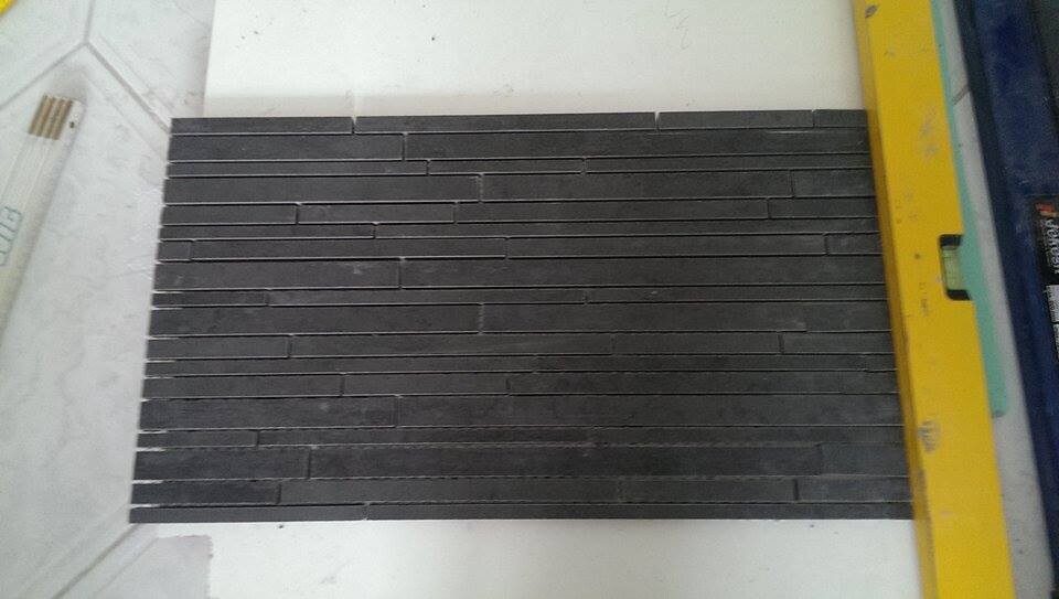 Sample of dark, narrow wall tiles on a white work surface with a yellow spirit level.