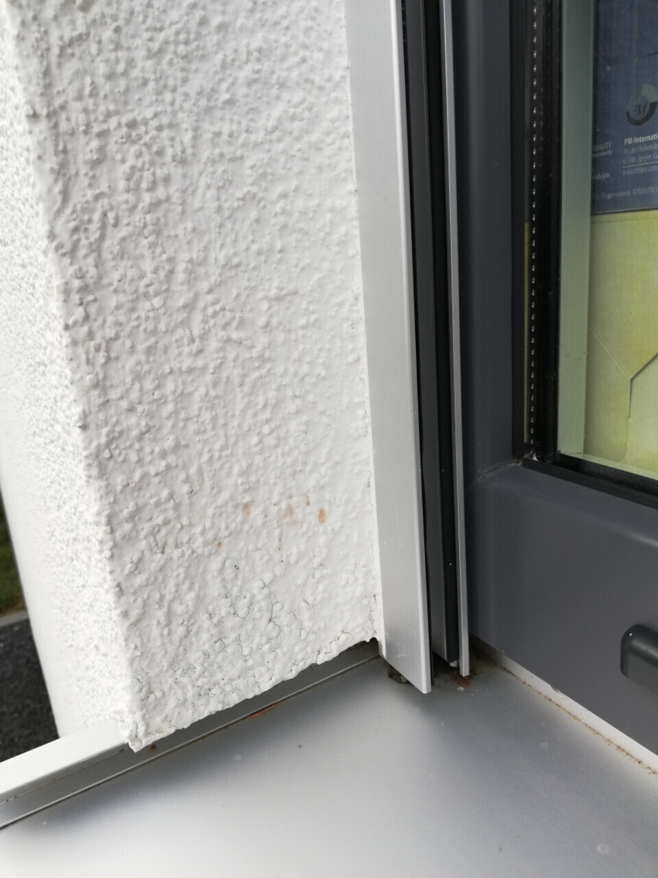 White, roughly textured exterior plaster next to gray window frame, rust stains at the bottom.