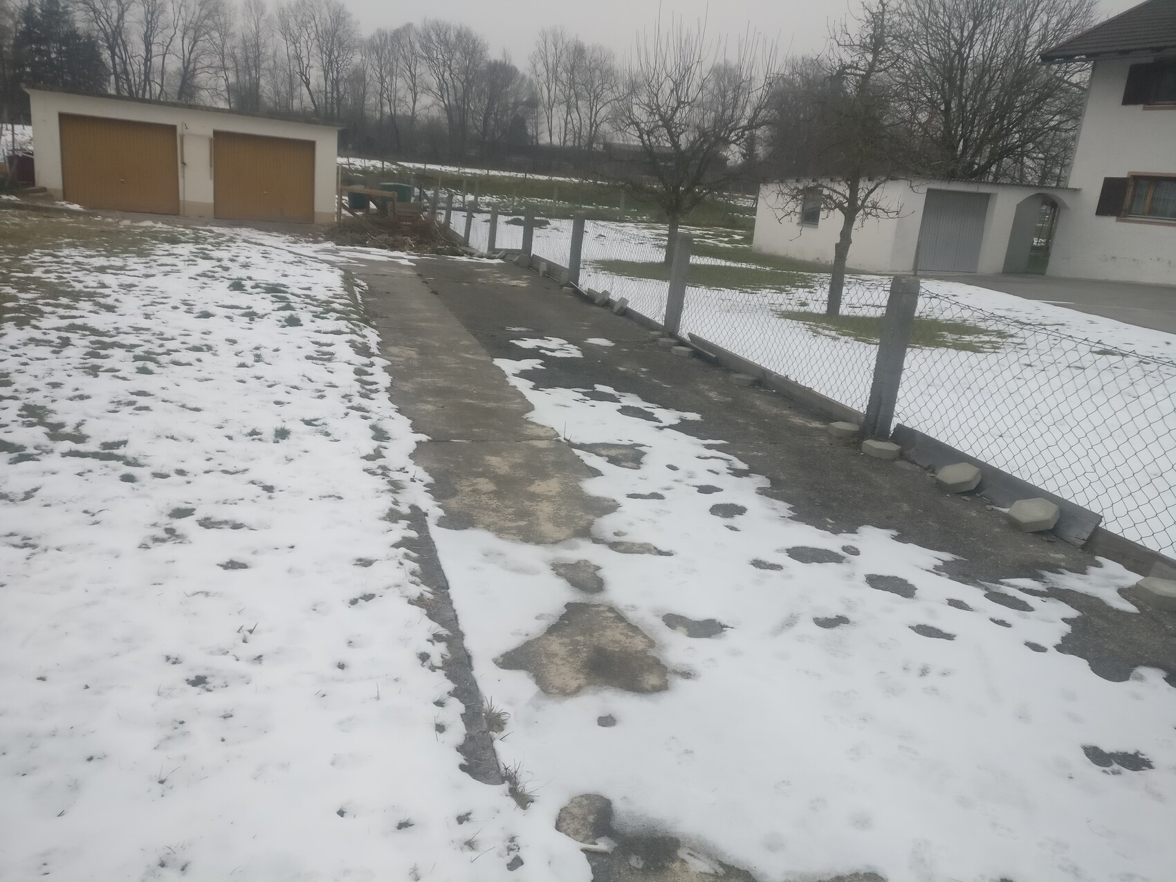 Exterior view of a residential house with garage, driveway, fence, and snow-covered forecourt in winter
