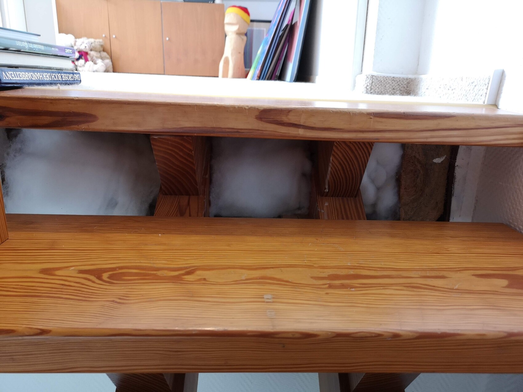 Wooden staircase with open construction opening below, visible insulation, bookshelves in the background.