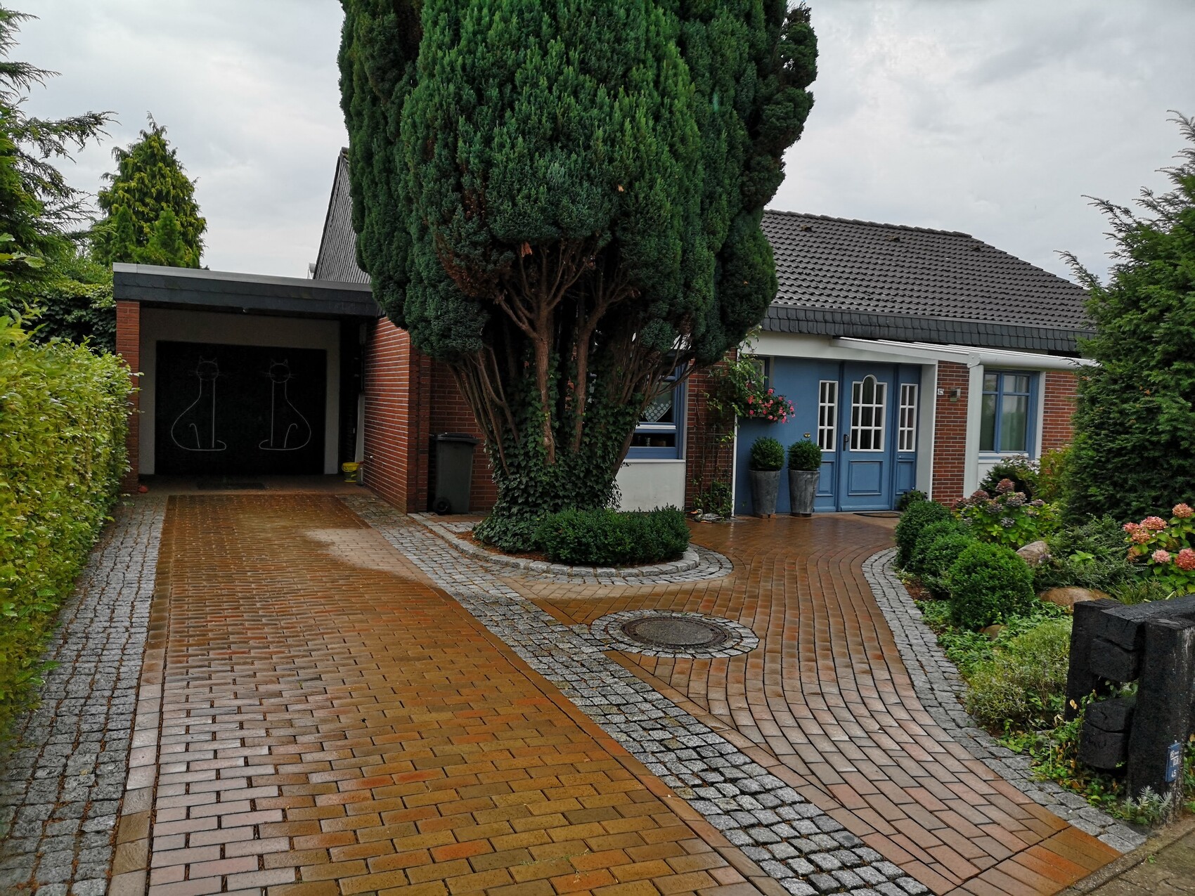 Front view of a house with blue entrance, large tree, paved driveway, and garden