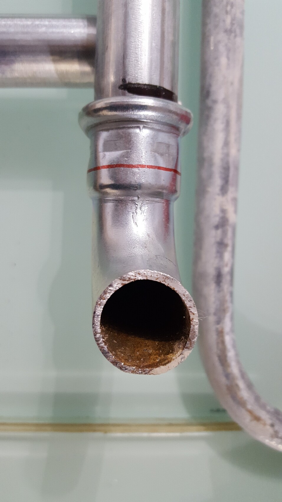 Open metal pipe with round opening, rust inside, and red ring at the connection.