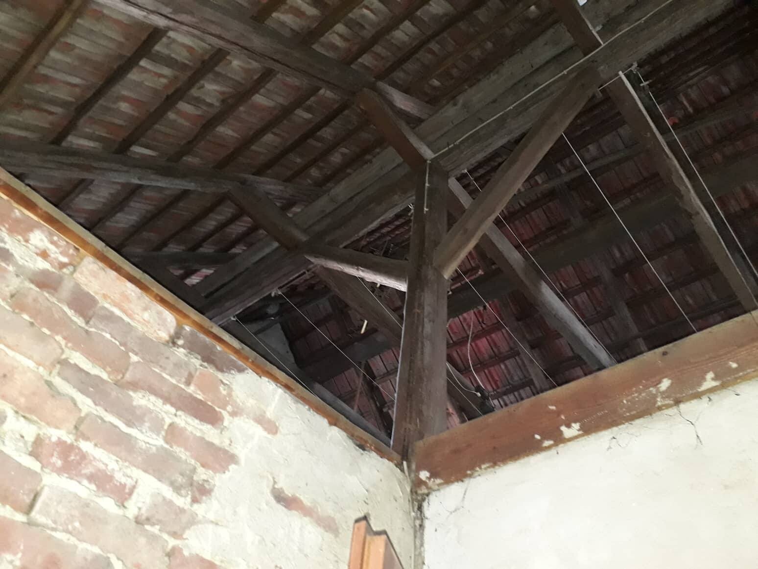 Dachboden mit sichtbaren Holzbalken, Ziegeldecke und bröckelnden Wänden.