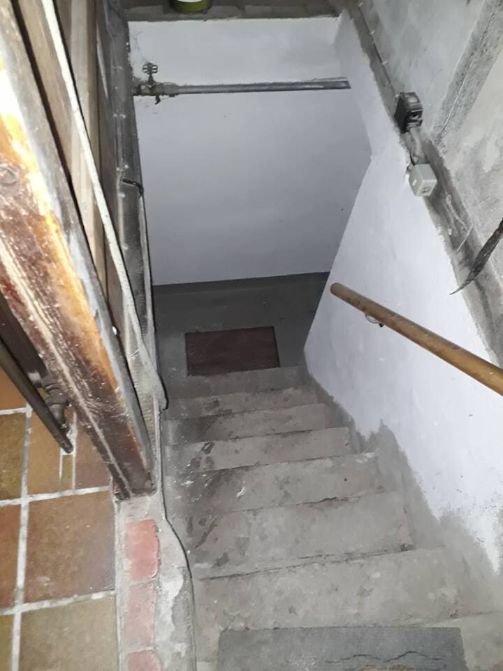 Enge Kellertreppe aus Beton mit Holzhandlauf an der Wand, unten dunkler Bereich.