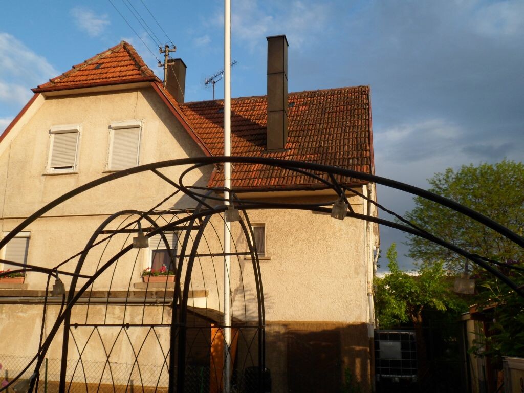 Exterior view of a house with a red tiled roof, windows, and garden in the foreground.